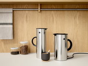 Zwei Edelstahl-Wasserkocher EM77 mit schwarzem Griff und Deckel, auf einer Küchenarbeitsplatte vor einer Holzwand, aus seitlicher Perspektive.