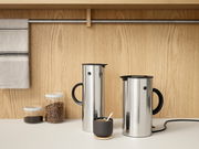 Zwei Edelstahl-Wasserkocher EM77 mit schwarzem Griff und Deckel, auf einer Küchenarbeitsplatte vor einer Holzwand, aus seitlicher Perspektive.