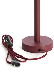 Nahaufnahme eines bordeauxroten Lampenfußes mit rundem Sockel und passendem Kabel mit Schalter und Stecker, seitliche Perspektive.