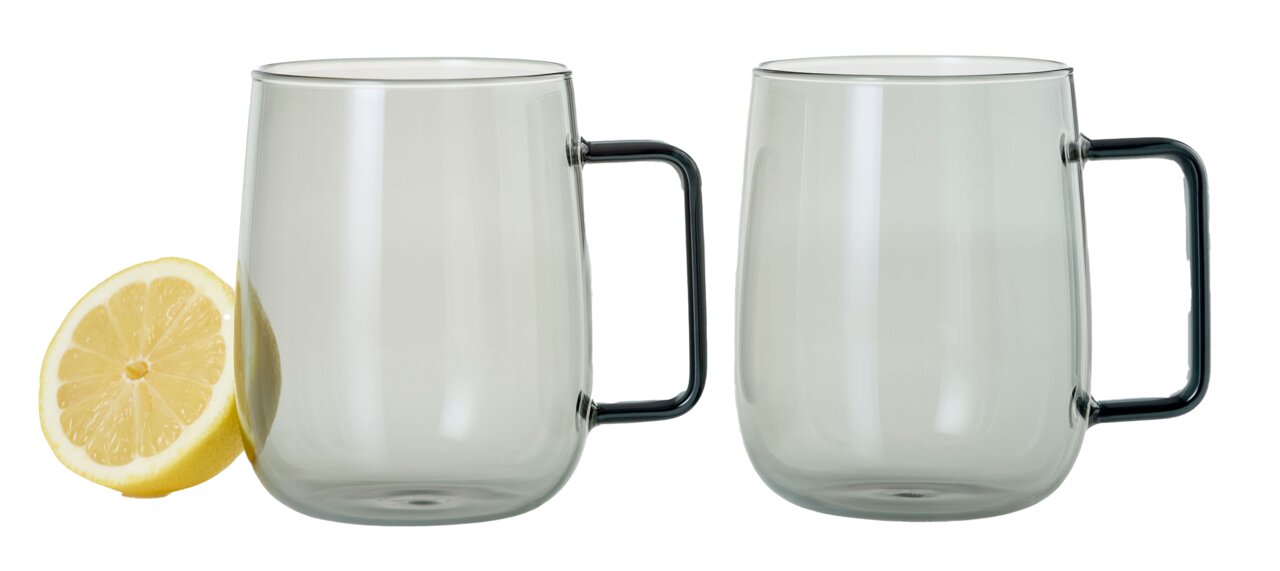 Zwei transparente Tassen mit schwarzen Griffen, frontal abgebildet, neben einer halben Zitrone.