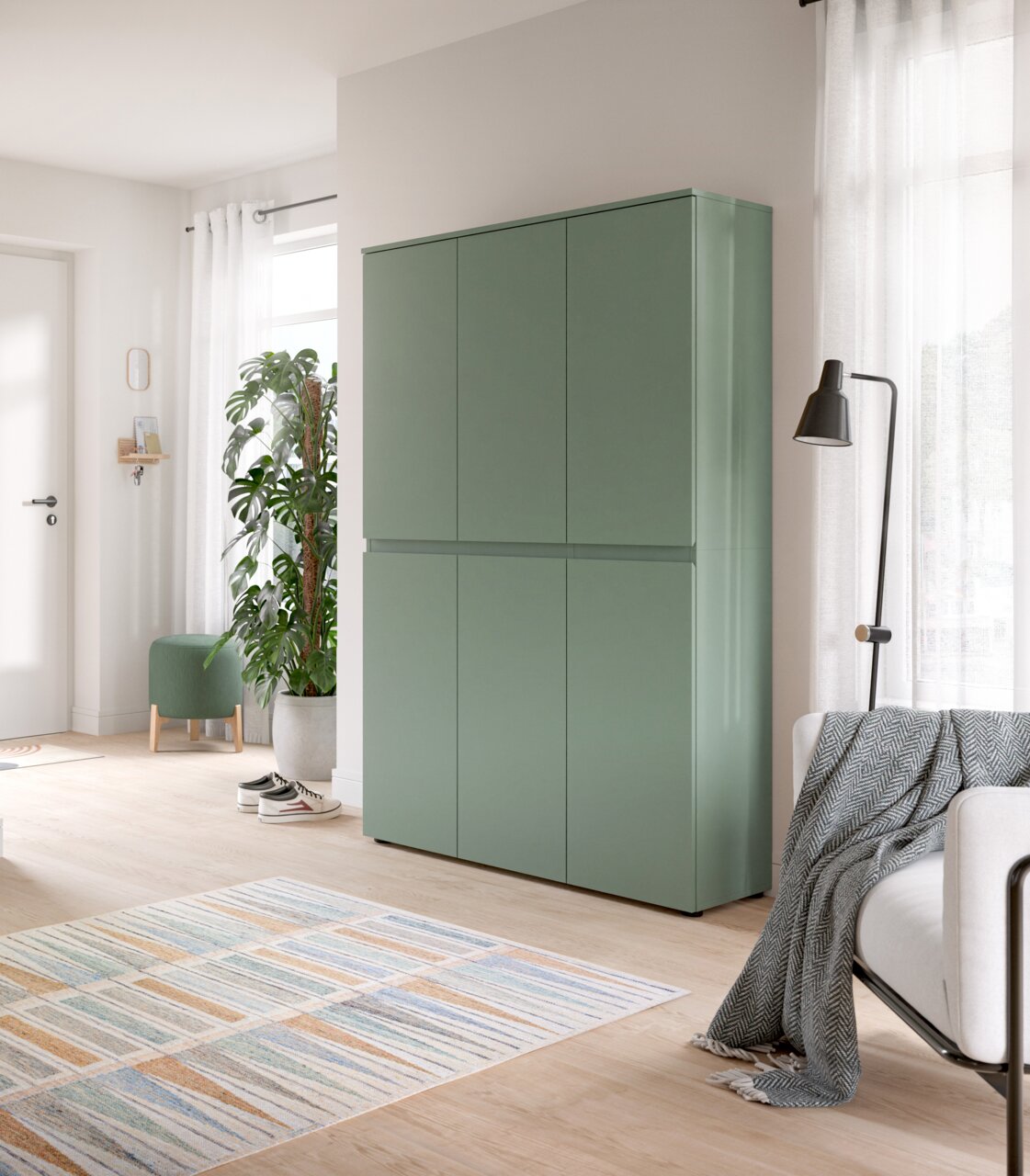 Salbeigrüner, minimalistischer Schrank mit vier grifflosen Türen in einem hellen Wohnraum, frontal aus leicht seitlicher Perspektive fotografiert.