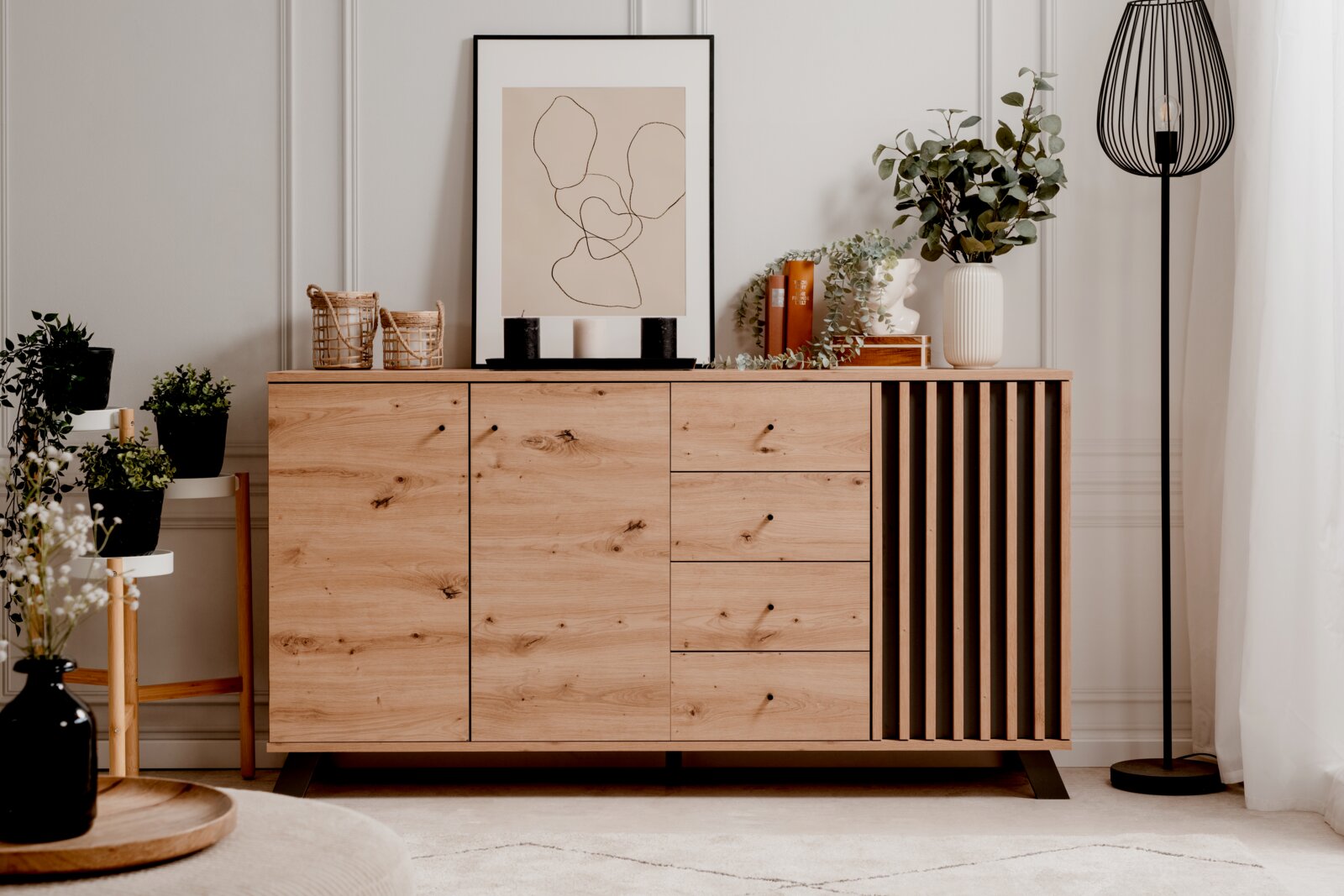 Modernes Sideboard aus Holz mit Schubladen und Türen, dekoriert mit Pflanzen und Kunstobjekten, frontal fotografiert.