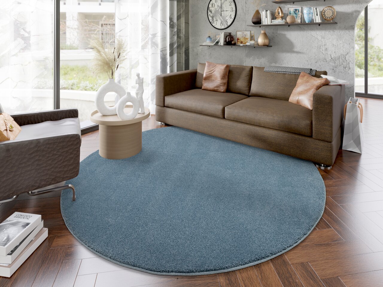 Runder, blauer Uni-Teppich in einem modernen Wohnzimmer mit braunem Sofa und Holzboden, aus der Vogelperspektive betrachtet.