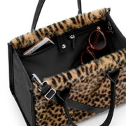 Schwarze Handtasche mit Leopardenfell-Optik und Reißverschlussfächern, mit sichtbarem Smartphone und Brille, aufgenommen in schräger Nahaufnahme von oben.