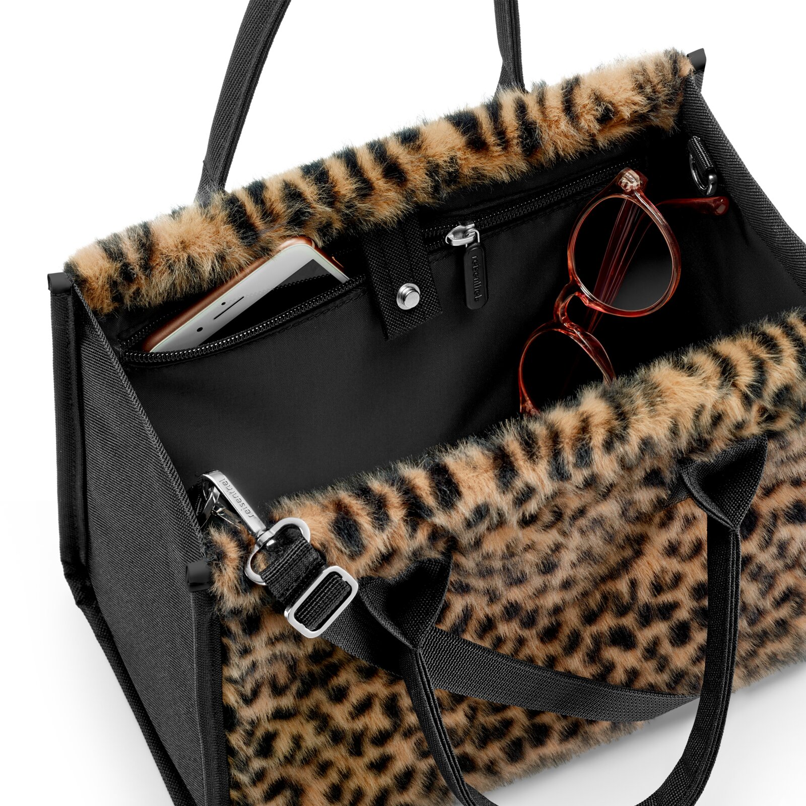 Schwarze Handtasche mit Leopardenfell-Optik und Reißverschlussfächern, mit sichtbarem Smartphone und Brille, aufgenommen in schräger Nahaufnahme von oben.