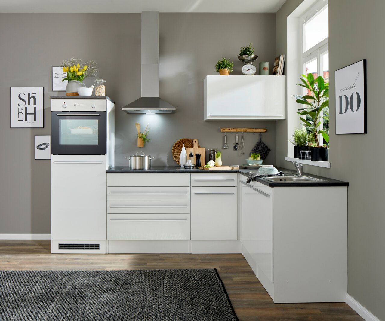 Moderne weiße Küche mit Eckunterschrank, Blick von vorne, ausgestattet mit Backofen, Dunstabzugshaube und Spüle, dekoriert mit Pflanzen und Küchenutensilien.