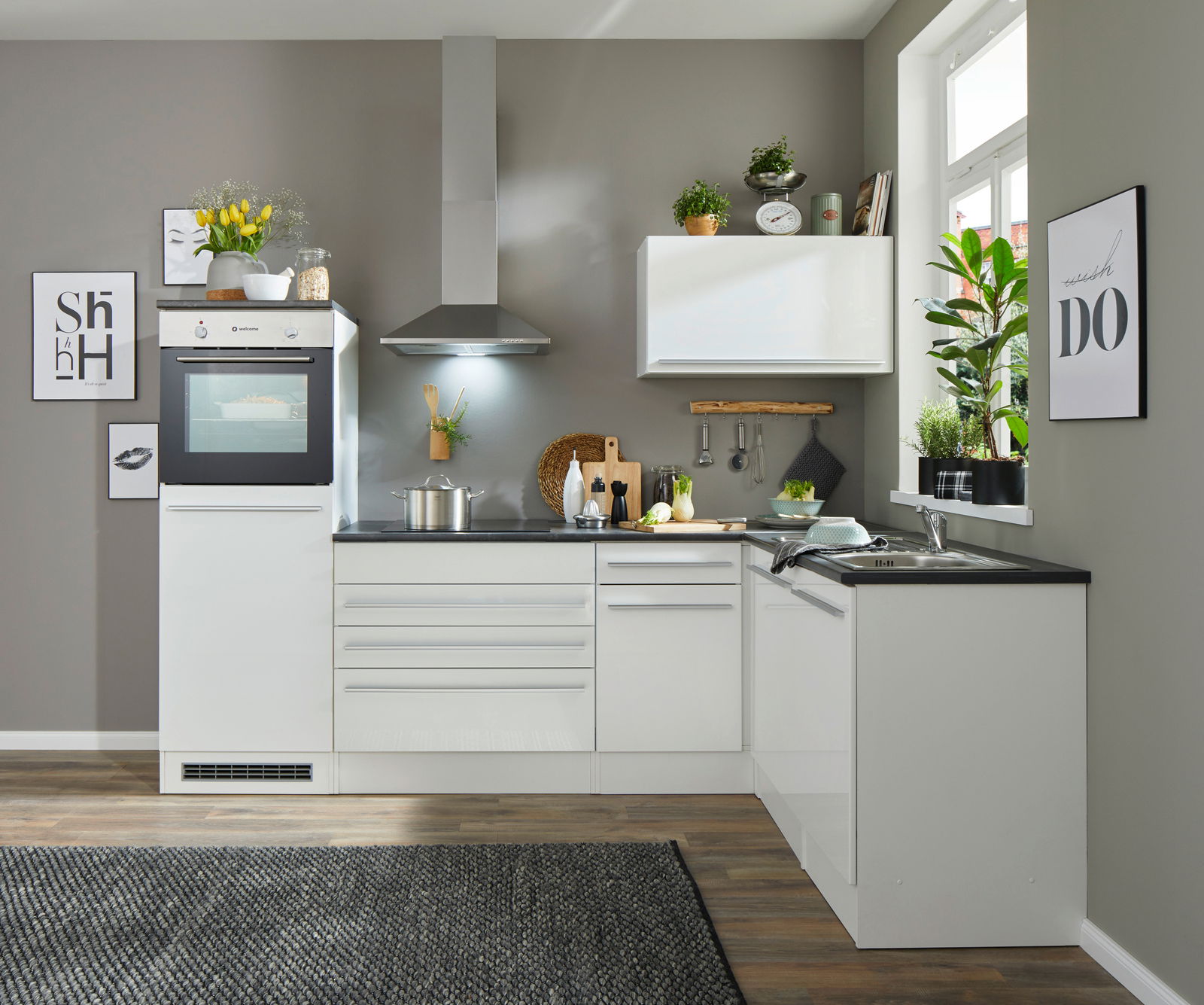 Moderne weiße Küche mit Eckunterschrank, Blick von vorne, ausgestattet mit Backofen, Dunstabzugshaube und Spüle, dekoriert mit Pflanzen und Küchenutensilien.