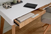 Moderner Schreibtisch mit weißer Oberfläche und Holzbeinen, aus der Perspektive von oben fotografiert. Eine Schublade ist teilweise geöffnet und zeigt darin liegende Ordner.