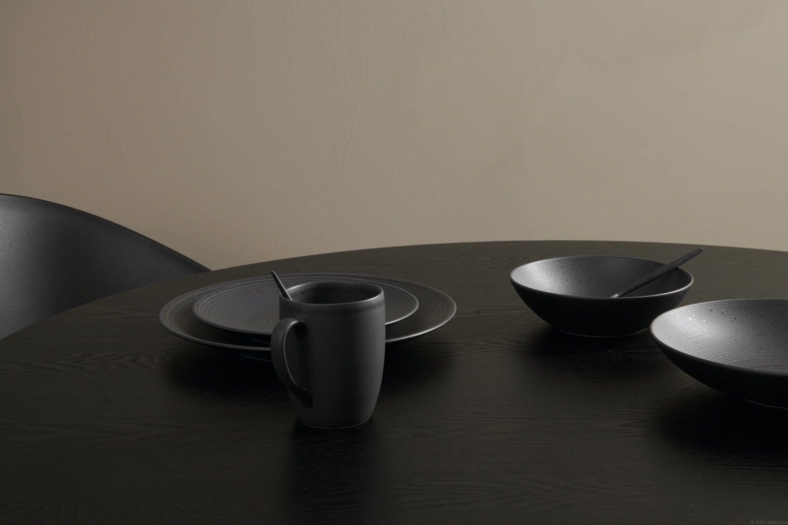 Schwarzes Kombiservice Bella Vista 24-teilig auf einem Tisch, bestehend aus Tellern, Schalen und einer Tasse, aus seitlicher Perspektive fotografiert.