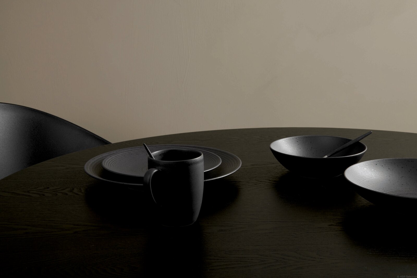 Schwarzes Kombiservice Bella Vista 24-teilig auf einem Tisch, bestehend aus Tellern, Schalen und einer Tasse, aus seitlicher Perspektive fotografiert.