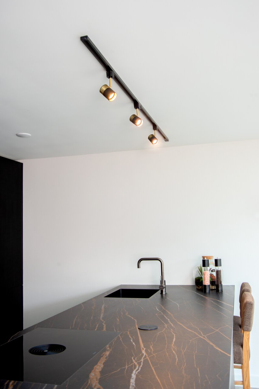 Deckenstrahler FLORIS in Schwarz mit drei verstellbaren Leuchten, montiert über einer modernen Kücheninsel. Perspektive von unten nach oben.