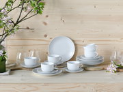 Kaffeeservice 18-teilig in eleganter Anordnung auf einem Holztisch, mit weißen Tassen und Tellern, umgeben von blühenden Zweigen, aus frontaler Perspektive.