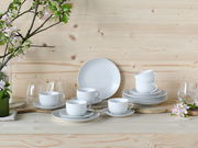 Kaffeeservice 18-teilig in eleganter Anordnung auf einem Holztisch, mit weißen Tassen und Tellern, umgeben von blühenden Zweigen, aus frontaler Perspektive.