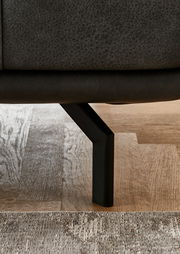 Nahaufnahme eines schwarzen Metallbeins eines Sofas auf einem Holzboden, seitliche Perspektive.