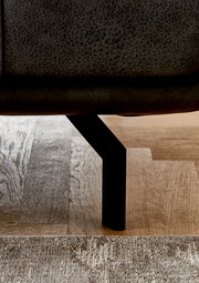 Nahaufnahme eines schwarzen Metallbeins eines Sofas auf einem Holzboden, seitliche Perspektive.