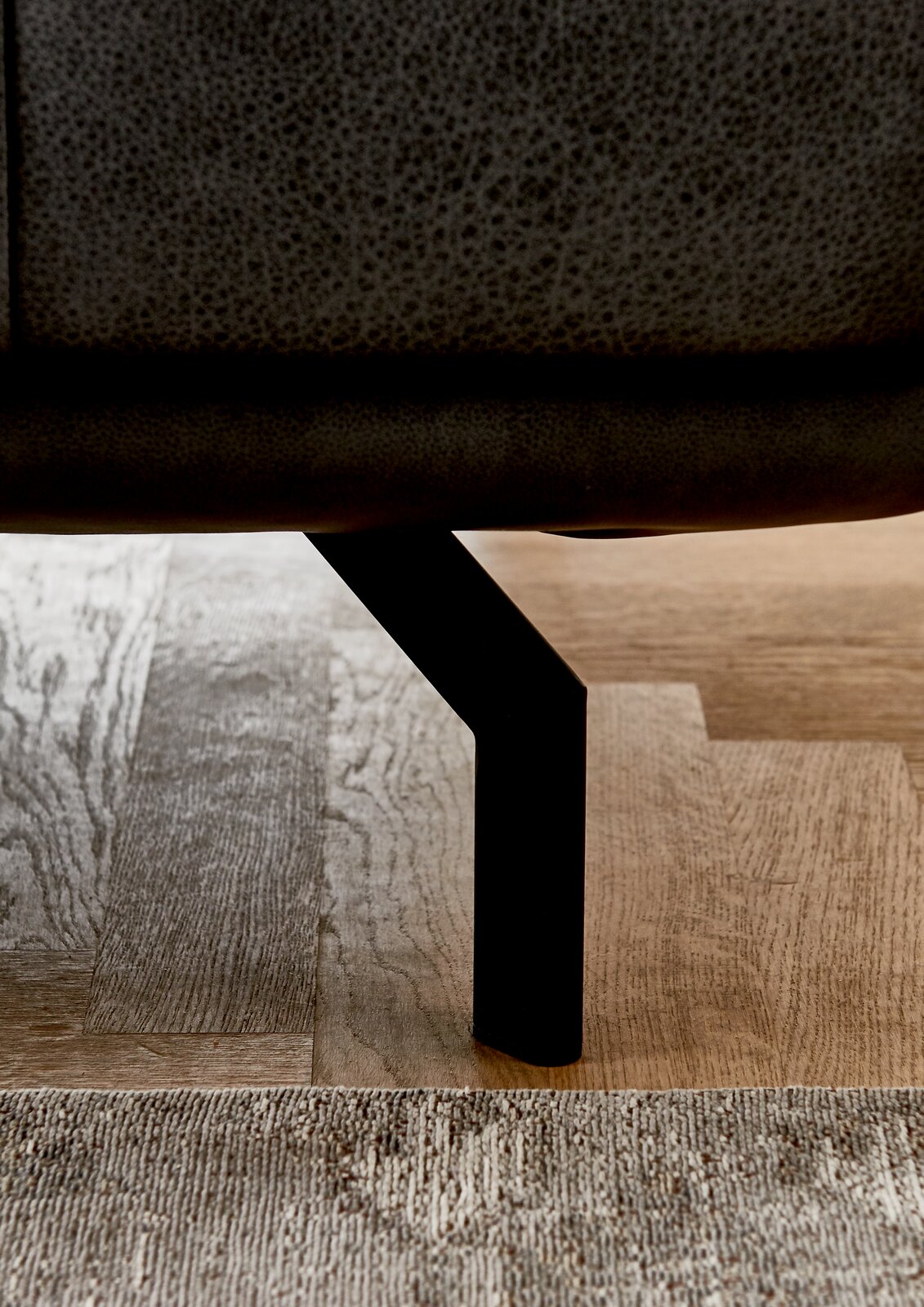 Nahaufnahme eines schwarzen Metallbeins eines Sofas auf einem Holzboden, seitliche Perspektive.