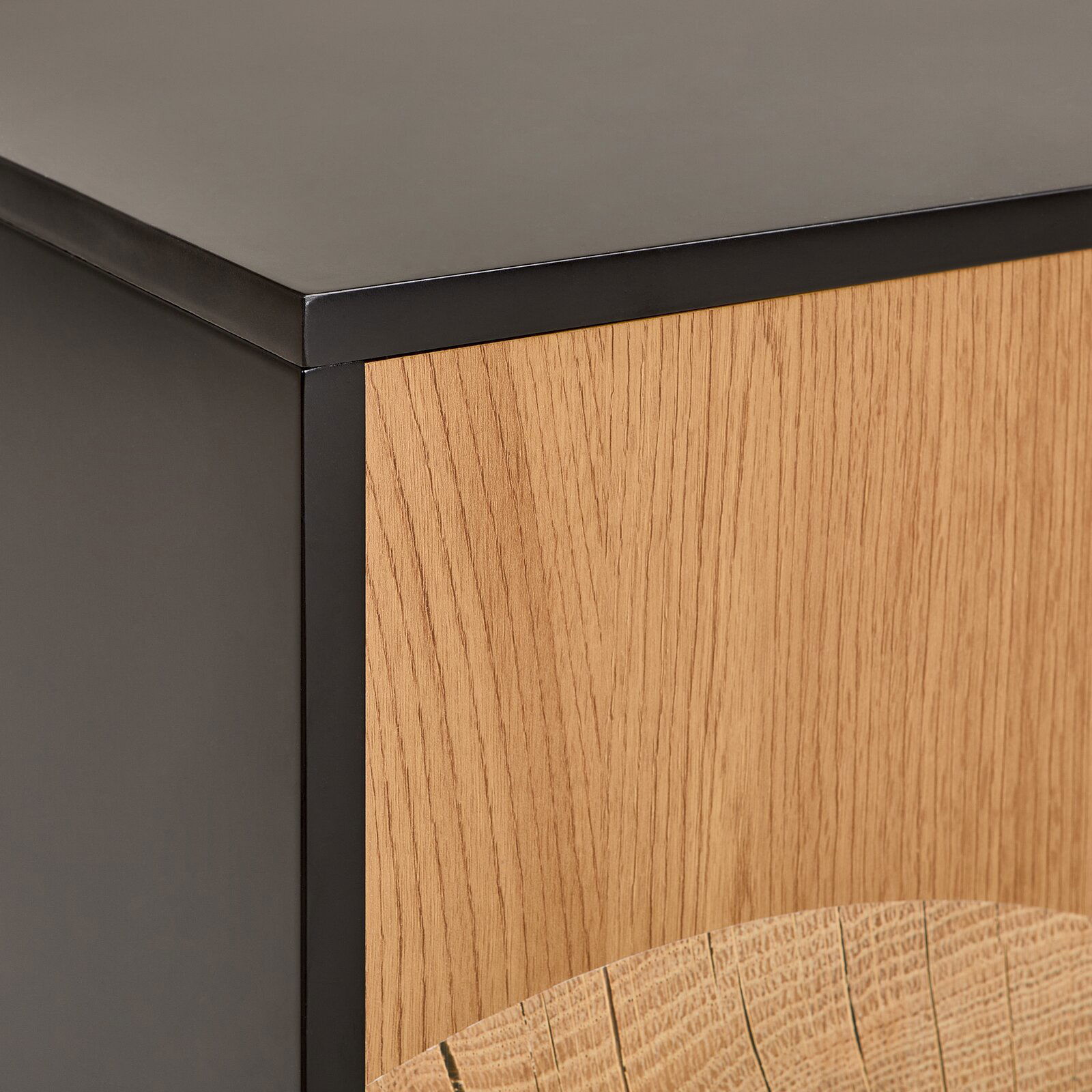 Detailaufnahme eines Möbelstücks mit mattschwarzem Metallrahmen und Front aus heller Eichenholz-Optik, fotografiert aus schräger Vorderansicht (Ecke/Detail).