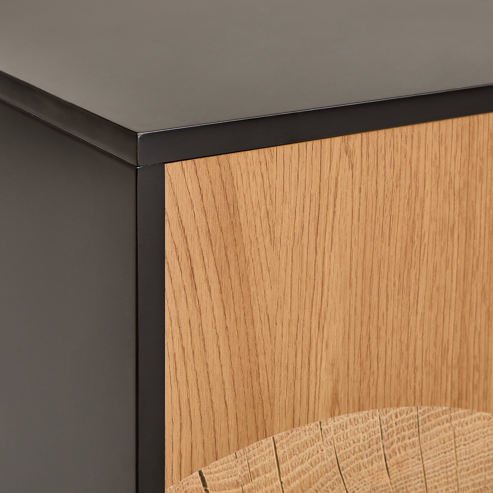 Detailaufnahme eines Möbelstücks mit mattschwarzem Metallrahmen und Front aus heller Eichenholz-Optik, fotografiert aus schräger Vorderansicht (Ecke/Detail).