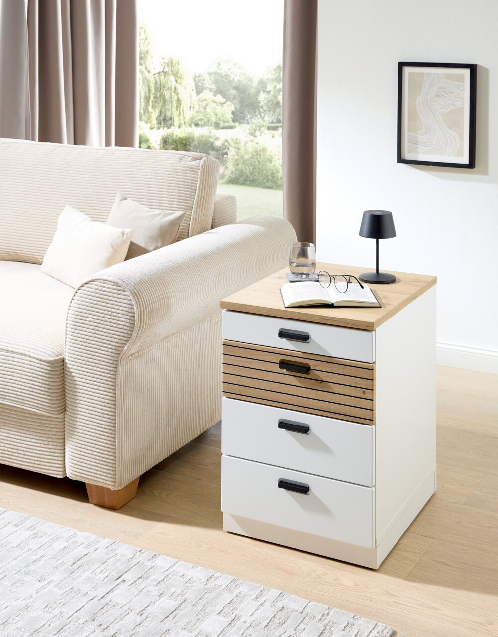 Rollcontainer GLENN in einem modernen Wohnzimmer, seitliche Perspektive, mit Holz- und weißen Elementen, neben einem Sofa platziert.