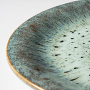 Detailaufnahme einer runden Keramikschale mit blau-grün gesprenkelter Glasur und braunem Rand, fotografiert aus schräger Draufsicht