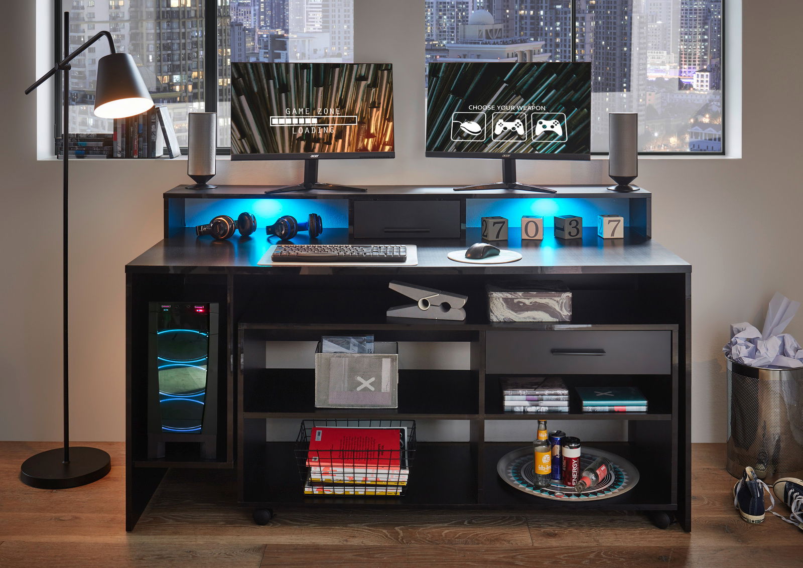 Gaming-Schreibtisch mit zwei Monitoren, Tastatur, Maus und Kopfhörern, beleuchtet von blauen LEDs, in einem modernen Raum mit Stadtblick.