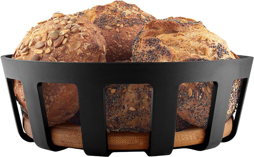 Zwarte broodmand met houten bodem, gevuld met diverse meergranenbroodjes met zaden en pitten, gefotografeerd in frontaal zijaanzicht