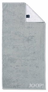 Graues Handtuch mit eingewebtem 'JOOP!' Logo, von oben fotografiert, mit umgeschlagener Ecke, die die weiße Rückseite zeigt.