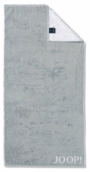 Graues Handtuch mit eingewebtem 'JOOP!' Logo, von oben fotografiert, mit umgeschlagener Ecke, die die weiße Rückseite zeigt.