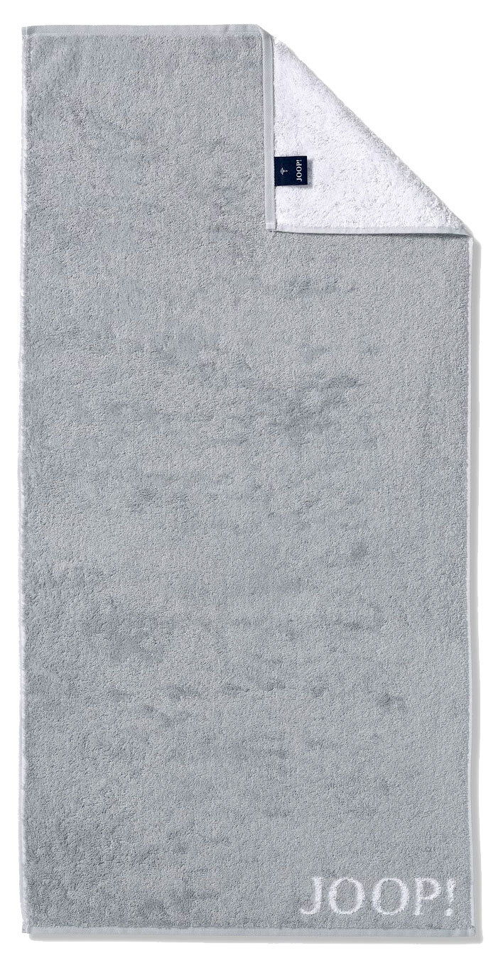 Graues Handtuch mit eingewebtem 'JOOP!' Logo, von oben fotografiert, mit umgeschlagener Ecke, die die weiße Rückseite zeigt.