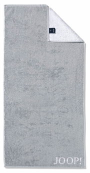 Graues Handtuch mit eingewebtem 'JOOP!' Logo, von oben fotografiert, mit umgeschlagener Ecke, die die weiße Rückseite zeigt.