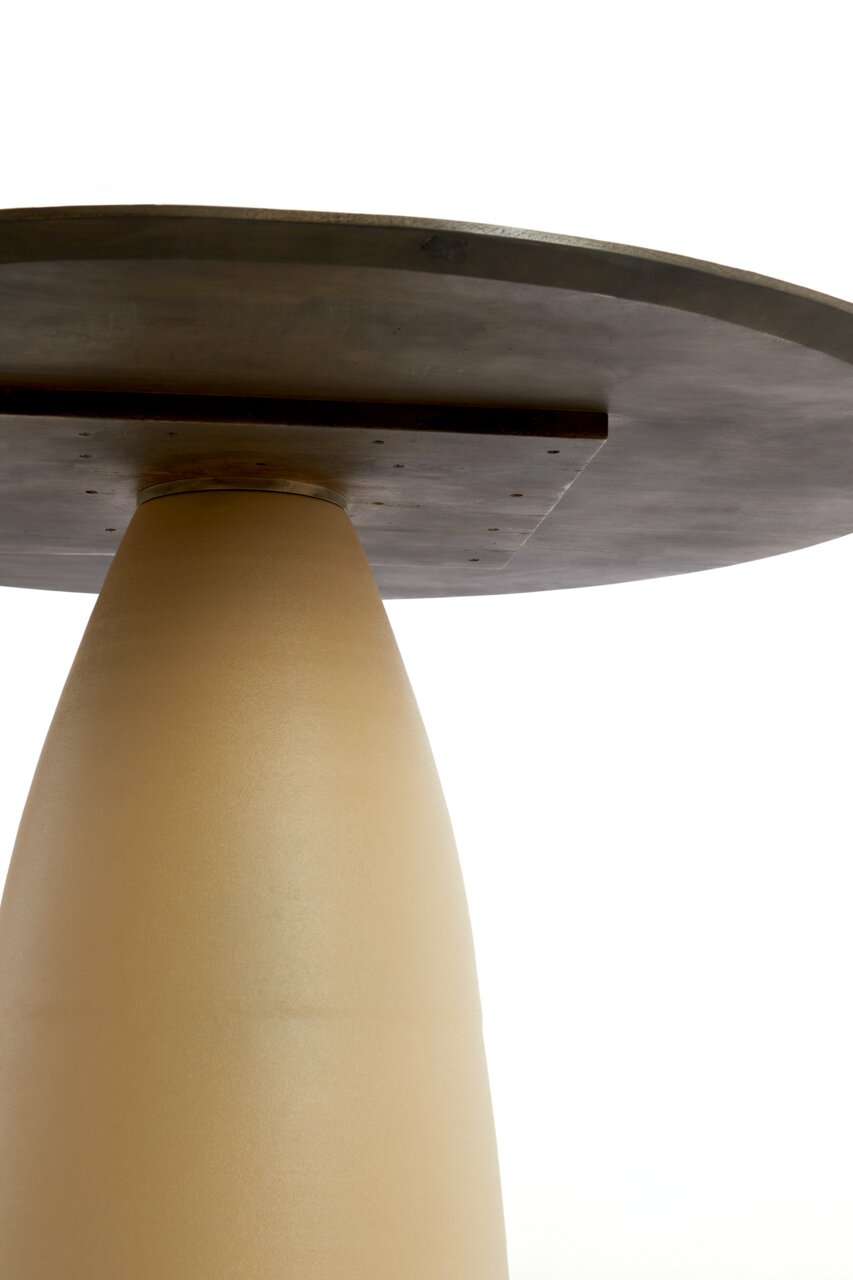 Close-up van een eettafel van onderaf, met een conische, beige voet en een donker tafelblad.