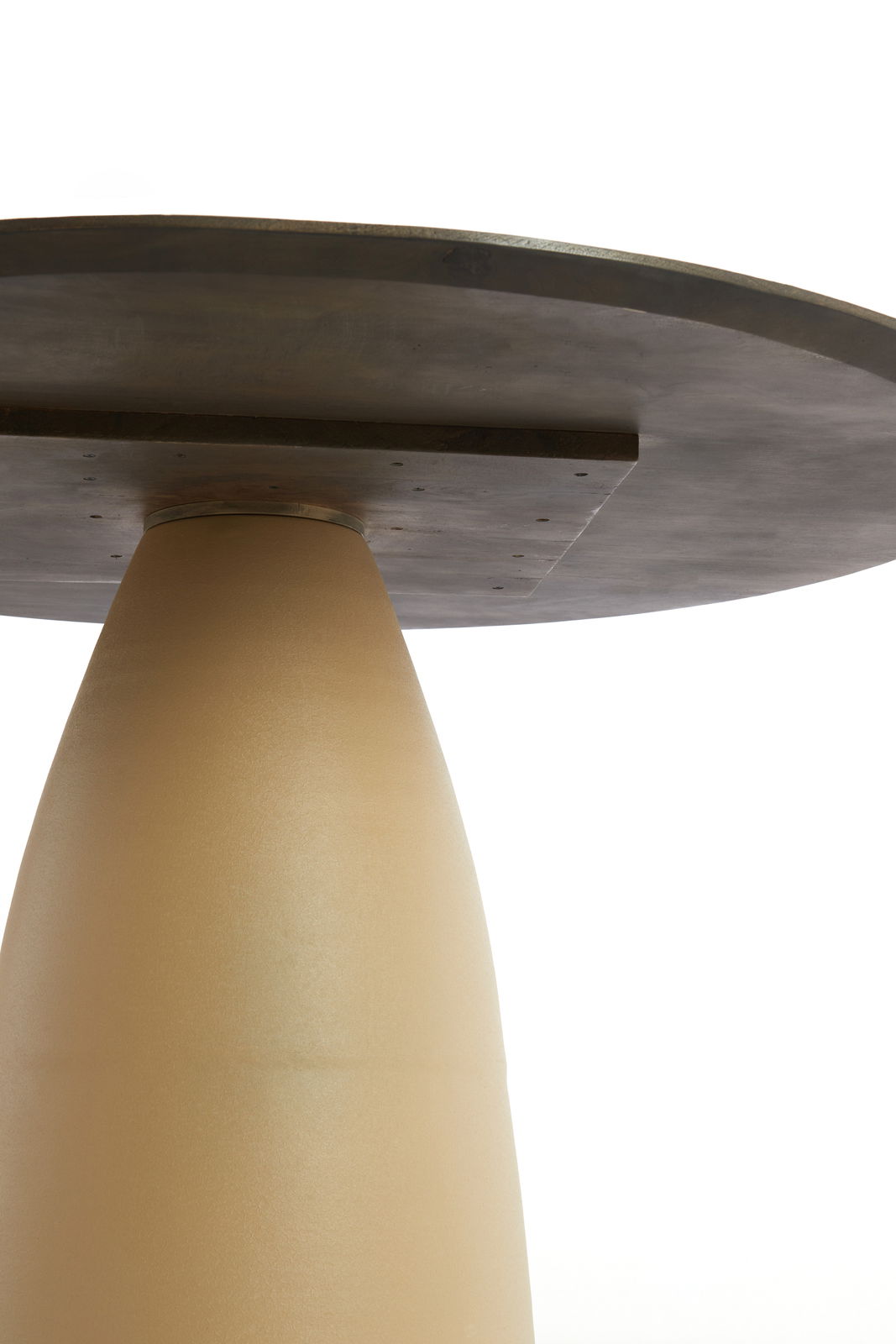 Nahaufnahme eines Esstisches von unten, mit einem konischen, beigen Sockel und einer dunklen Tischplatte.