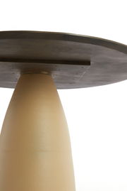 Nahaufnahme eines Esstisches von unten, mit einem konischen, beigen Sockel und einer dunklen Tischplatte.