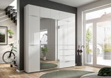 Moderner weißer Kleiderschrank mit Spiegeltüren und Schubladen, perspektivisch von vorne rechts fotografiert, in einem hellen Raum mit großen Fenstern.