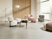 Moderne Wohnzimmermöbel in einem hellen Raum mit Sesseln, Hockern und Beistelltischen aus verschiedenen Stoffen und Farben, seitliche Perspektive.