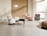 Moderne Wohnzimmermöbel in einem hellen Raum mit Sesseln, Hockern und Beistelltischen aus verschiedenen Stoffen und Farben, seitliche Perspektive.