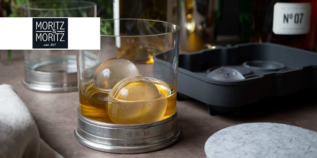 Ein Whiskeyglas mit zwei Eiskugeln daneben eine Eisform der Marke Moritz & Moritz