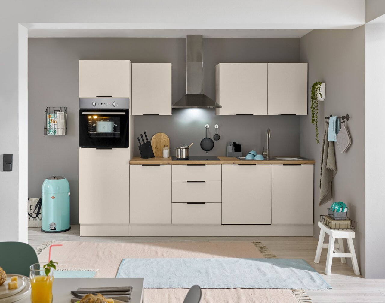 Moderne Küchenzeile in heller Farbe mit eingebautem Backofen, Dunstabzugshaube und Spüle, frontal betrachtet.