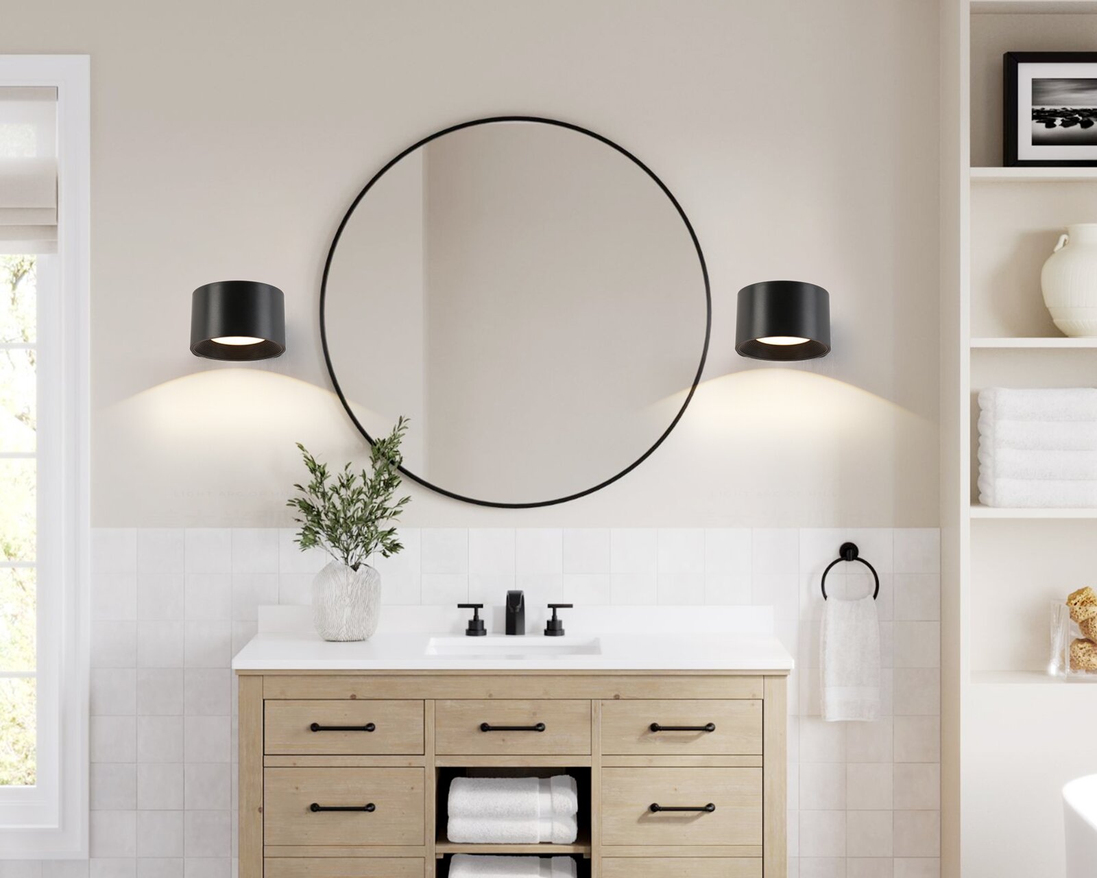 Runder Wandspiegel mit dünnem schwarzem Metallrahmen über einem Waschbecken, flankiert von zwei schwarzen zylindrischen Wandleuchten; Frontalansicht im Badezimmer
