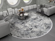Runder Designer Teppich in einem modernen Wohnzimmer mit grauen Sofas und einem runden Couchtisch, von oben betrachtet.
