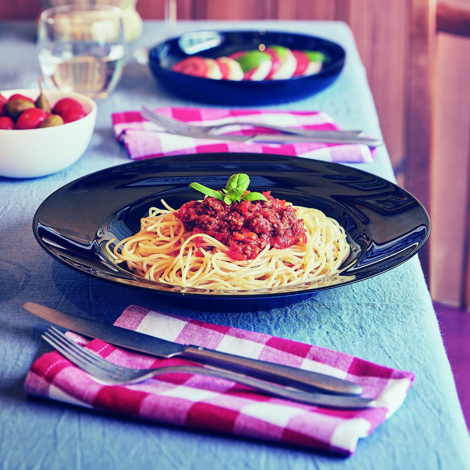 Creatable Pastateller 6-tlg ITALIEN PARTY Spaghetti mit Bolognese-Soße und Basilikum auf einem schwarzen Teller auf gedecktem Tisch, fotografiert in leicht schräger Perspektive von vorne