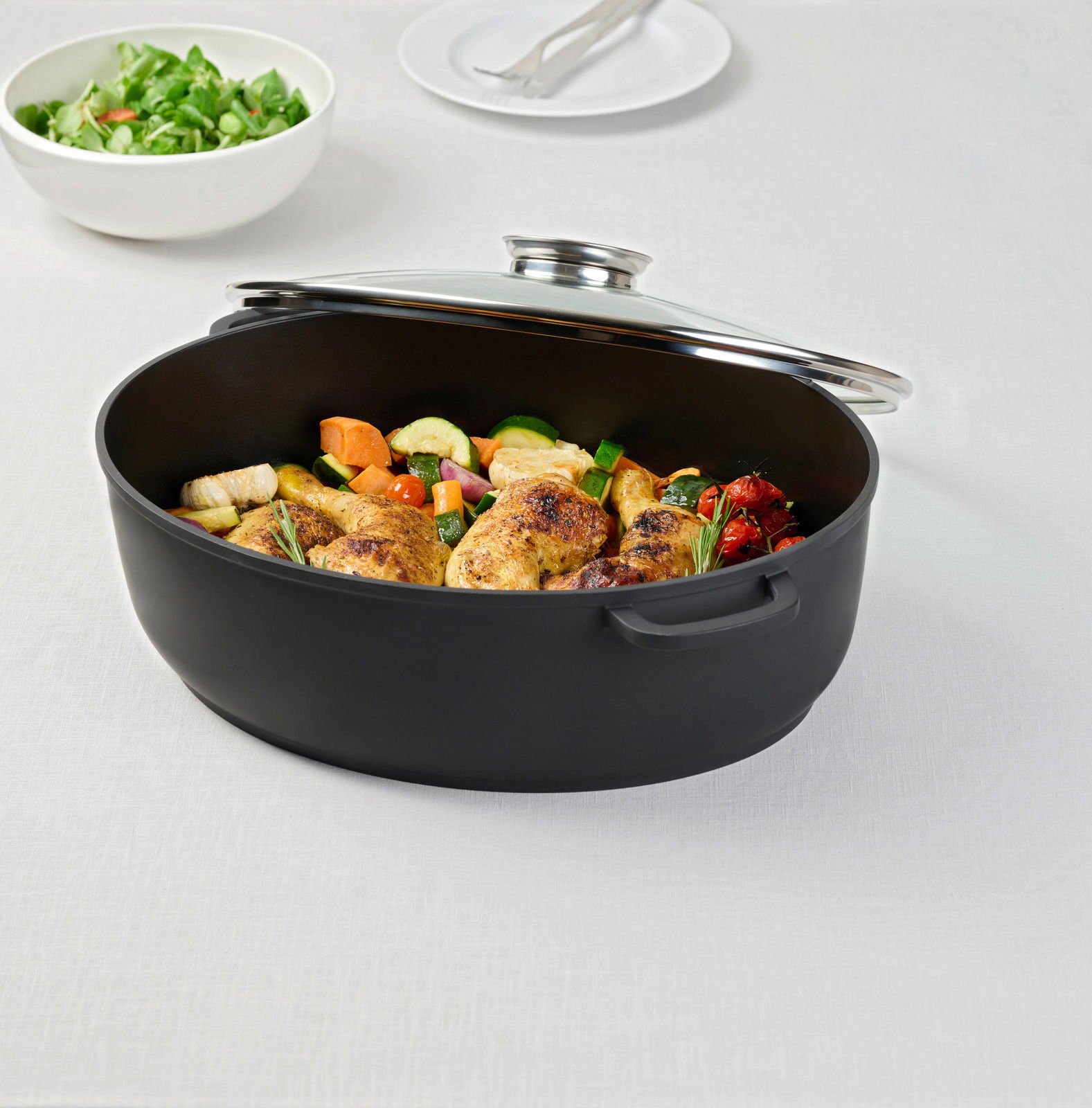 Homeware Bräter PERFECT COOKING Schwarzer Bräter mit Deckel, gefüllt mit gebratenem Hähnchen und Gemüse, auf einem Tisch von schräg oben fotografiert.