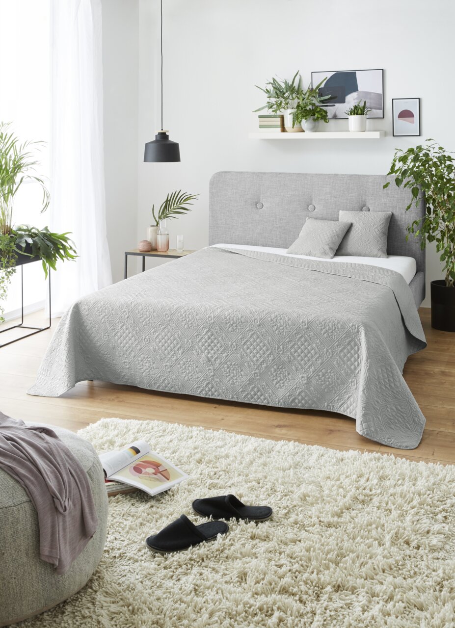 Graue Tagesdecke Nancy 220x250cm auf einem Bett in einem modernen Schlafzimmer, seitliche Perspektive.
