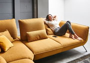 Frau entspannt auf einer senfgelben Eckgarnitur, seitliche Perspektive