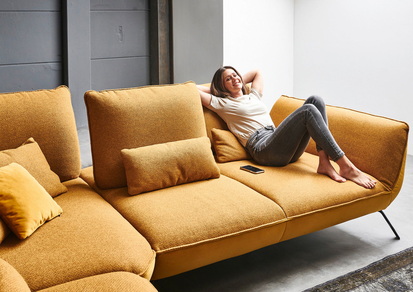 Frau entspannt auf einer senfgelben Eckgarnitur, seitliche Perspektive