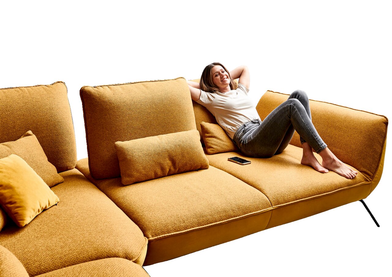 Frau entspannt auf einer senfgelben Eckgarnitur, seitliche Perspektive