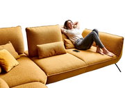 Frau entspannt auf einer senfgelben Eckgarnitur, seitliche Perspektive