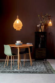 Runder Esstisch aus Holz mit zwei modernen Stühlen, einer in Grün und einer in Schwarz, auf einem gemusterten Teppich. Im Hintergrund eine stilvolle Hängelampe und eine dekorative Vitrine. Perspektive: Frontalansicht.