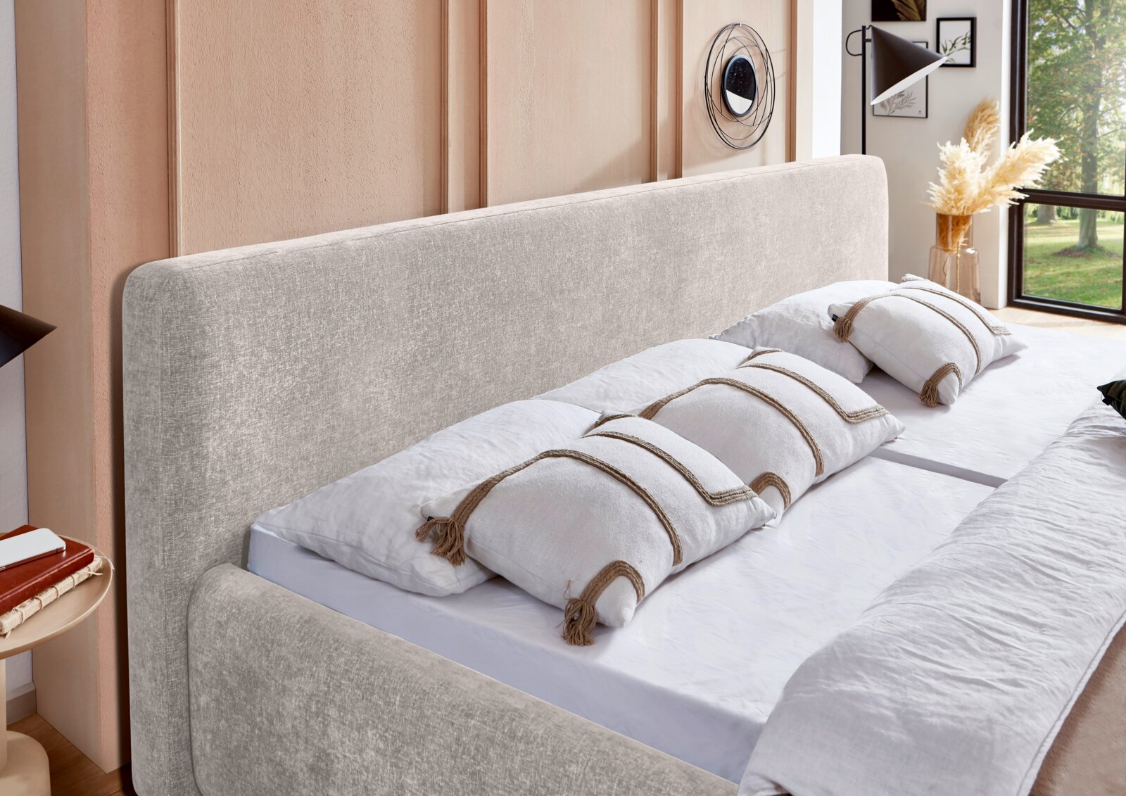 Modernes Doppelbett mit hohem, weich gepolstertem Kopfteil in hellem Beige, aus schräger Vorderansicht in einem stilvollen Schlafzimmer gezeigt