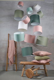 Mehrere runde Lampenschirme in verschiedenen Farben schweben in der Luft. Im Vordergrund sind eine Holzbank, ein Hocker und Kissen zu sehen. Die Perspektive ist leicht von unten.